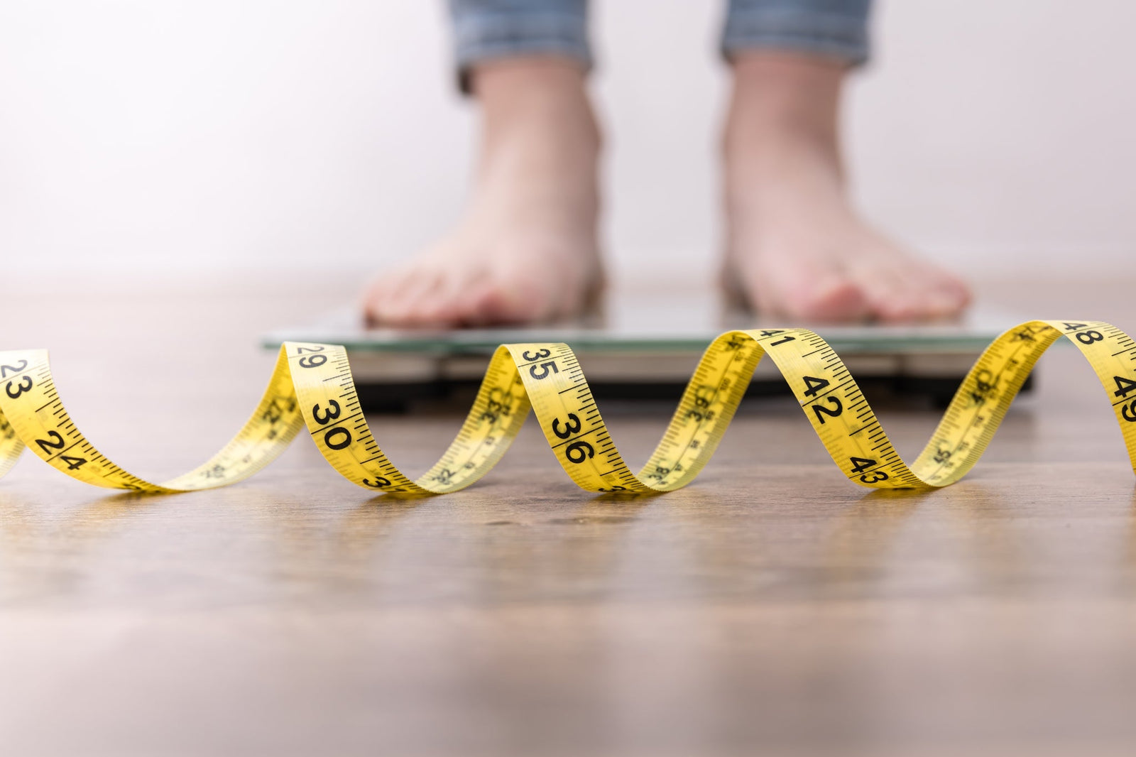 Feet standing on a scale with a yellow measuring tape on the ground