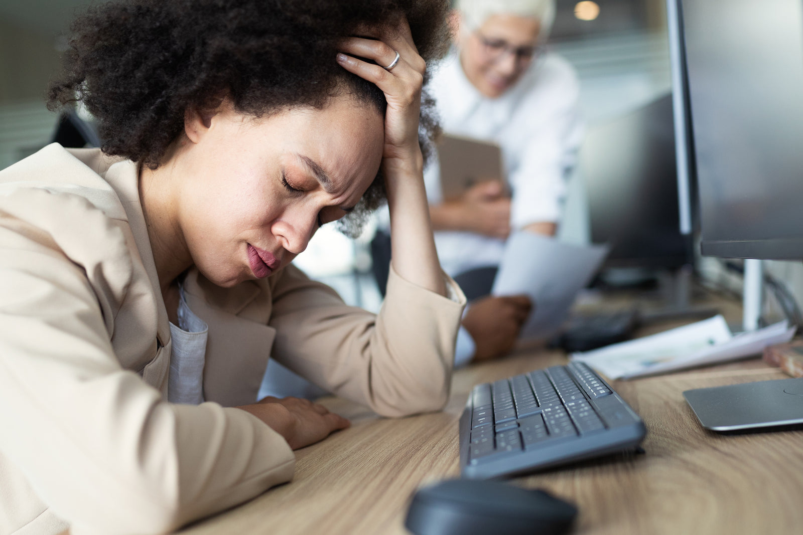A woman sits at her desk with her head in her hands in pain.