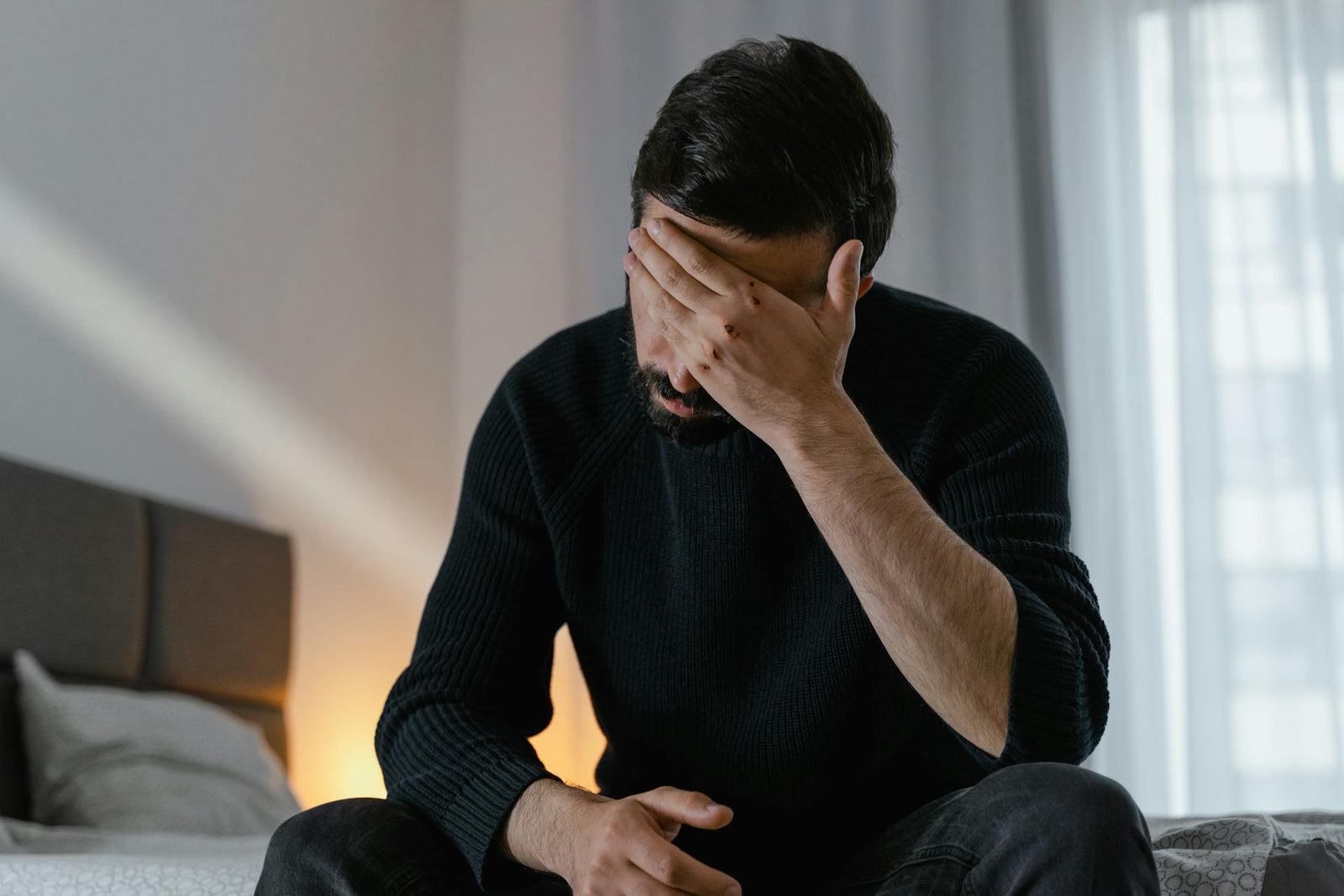A man sits in bed with his head in his hand.
