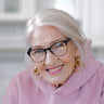 A woman in a pink sweatshirt and gold earrings poses.