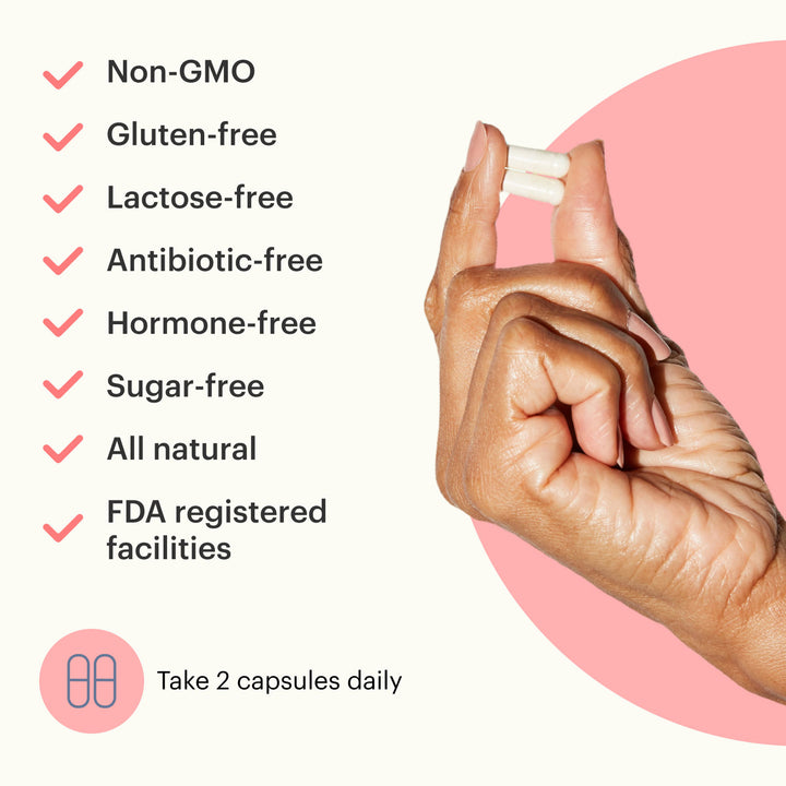 Hand holding Because Women's Probiotic supplement bottle with text "non-GMO, gluten-free, lactose-free, antibiotic-free, hormone-free, sugar-free, and all natural" on white and pink background
