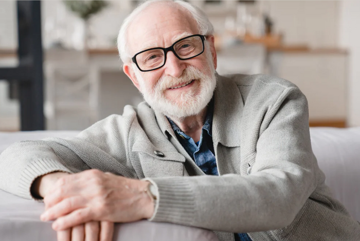 A man smiles while leaning on a couch.