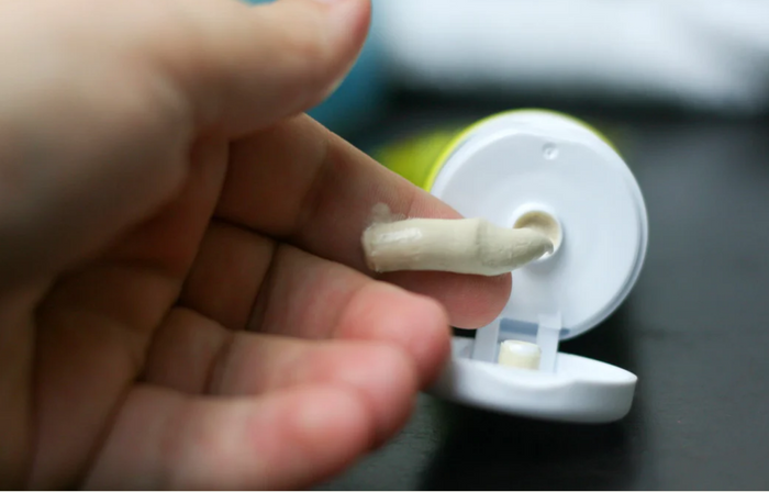 A person gathers some lotion from a tube.