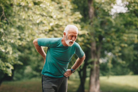 Older man in a green shirt on a run holding his lower back