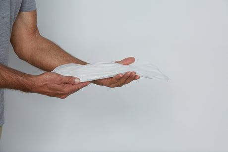 Man in dark grey t-shirt holding a Because booster pad in outstretched hands on a light grey background