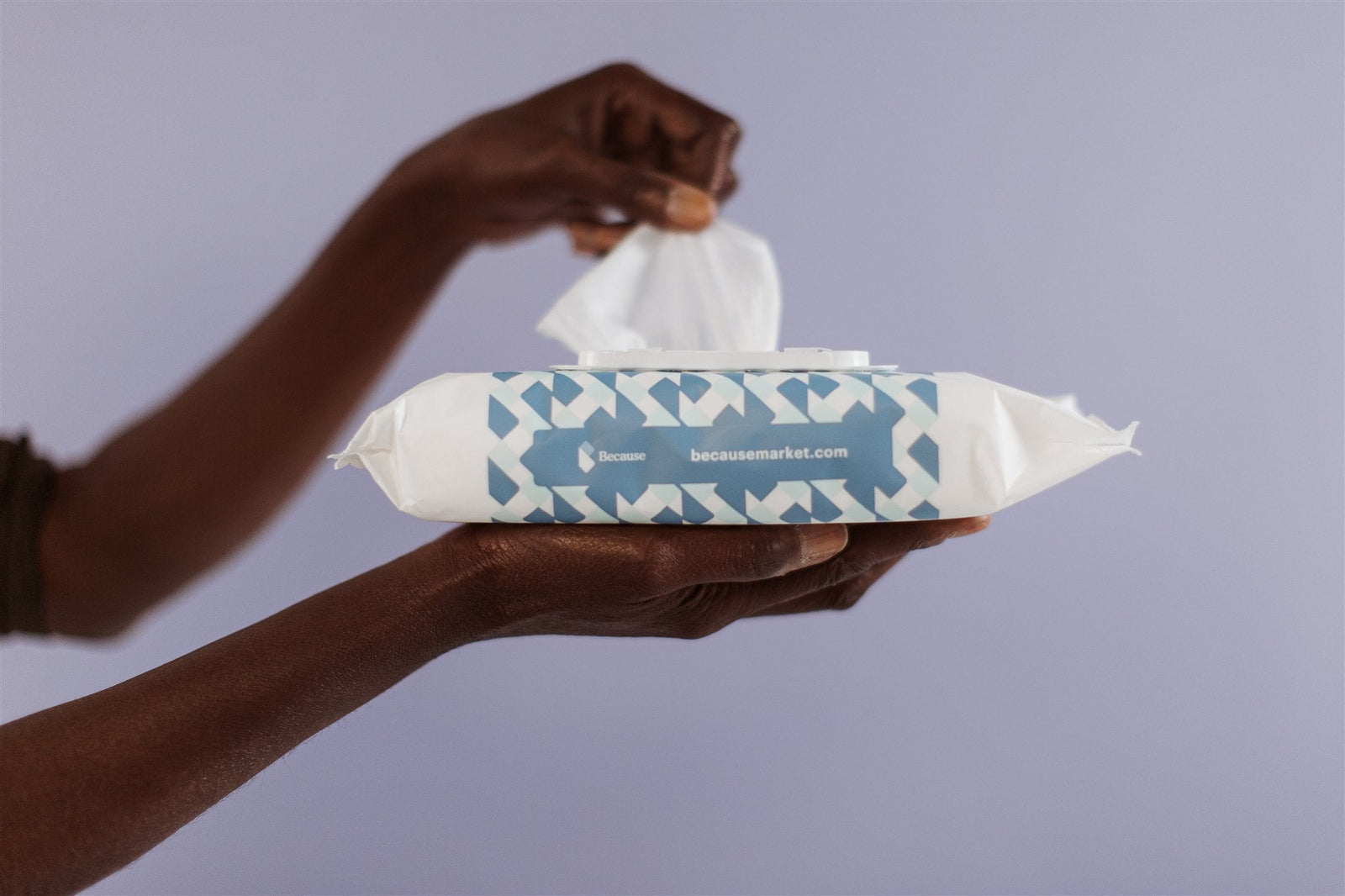 African American woman holding a pack of Because cleansing wipes and pulling a wipe from the pouch on a purple background. 