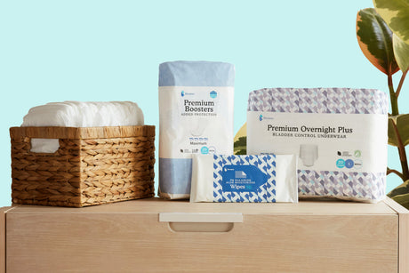 Packages of Because Overnight Underwear, Because Cleansing Wipes, and Because Booster pads sitting on top of a dresser with a basket filled with Because Overnight Underwear. Plant in background against blue wall 