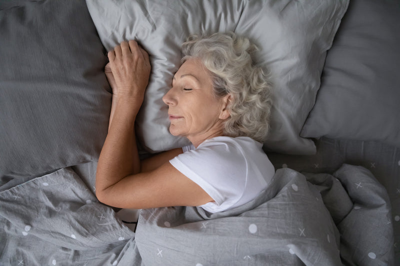 Older woman sleeping in bed with grey pillows and comforter