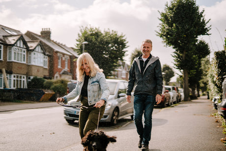 Older man and woman smiling while walking their dog in a city neighborhood