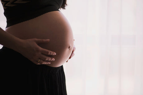 Pregnant woman wearing black shirt and bottoms holding her exposed belly in her hands with a blurred background