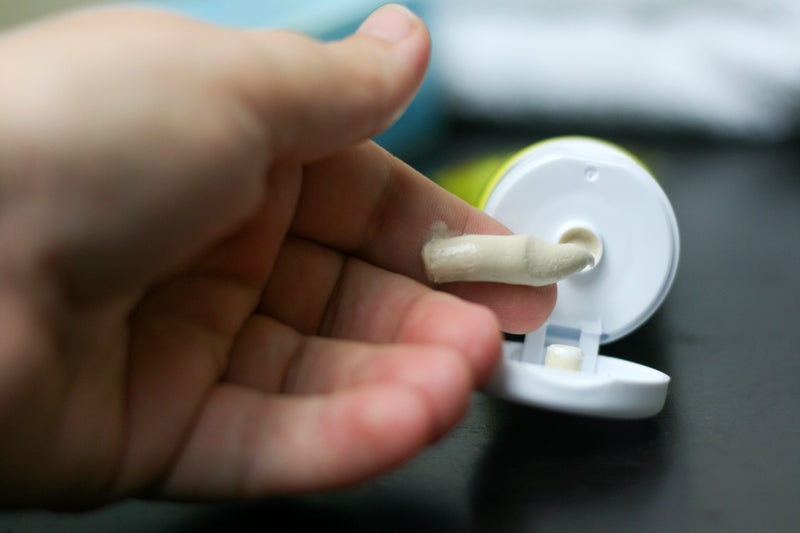 Hand with skin cream on finger tip with bottle in the background