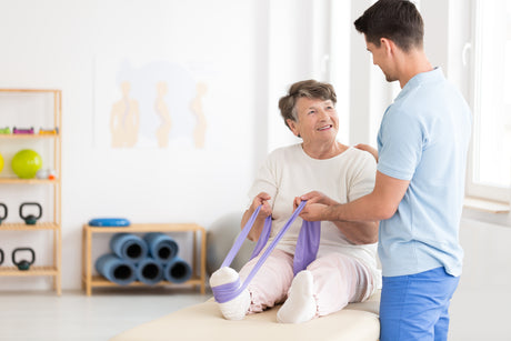 Older woman sitting with a physical therapist ready to do some knee exercises with a purple band