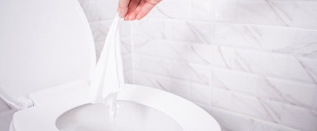 Close up hand throwing toilet paper to the toilet in a white tile bathroom.