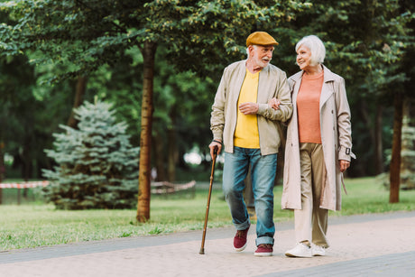 An older couple walking through the park. The man is walking with a standard cane