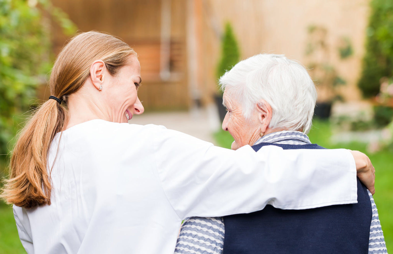 A female caregiver with her arm wrapped around an older woman's shoulders