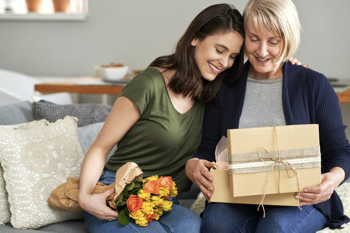 A mother daughter sitting on a couch opening a wrapped gift
