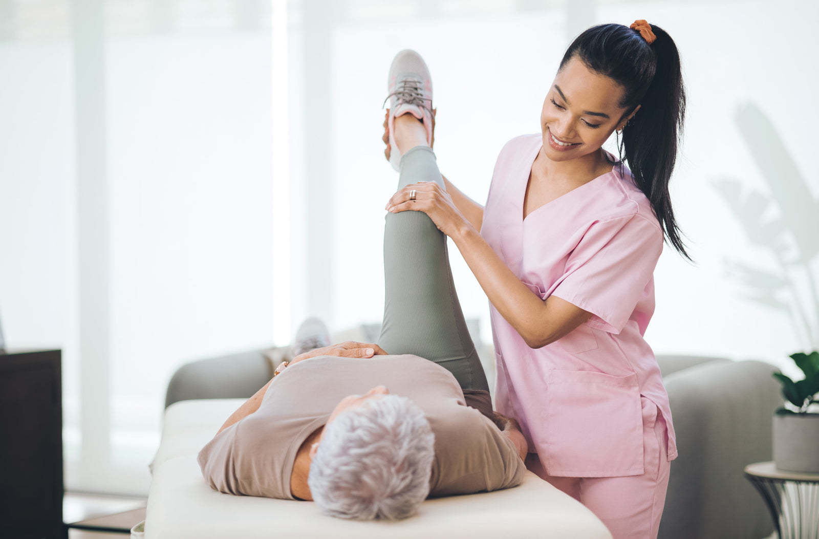 A physical therapist helping an older adult female stretch her leg on a massage table