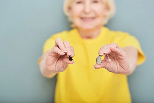 Woman in yellow shirt holding hearing aids in her hands