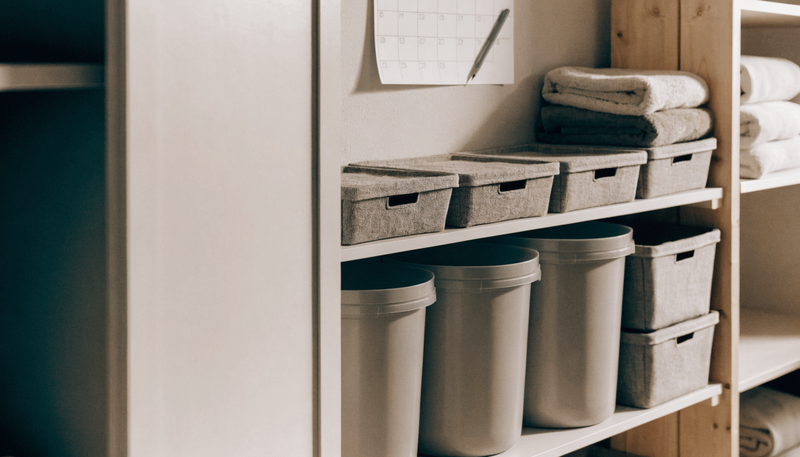 Organized shelf with storage bins, folded towels, and a wall calendar