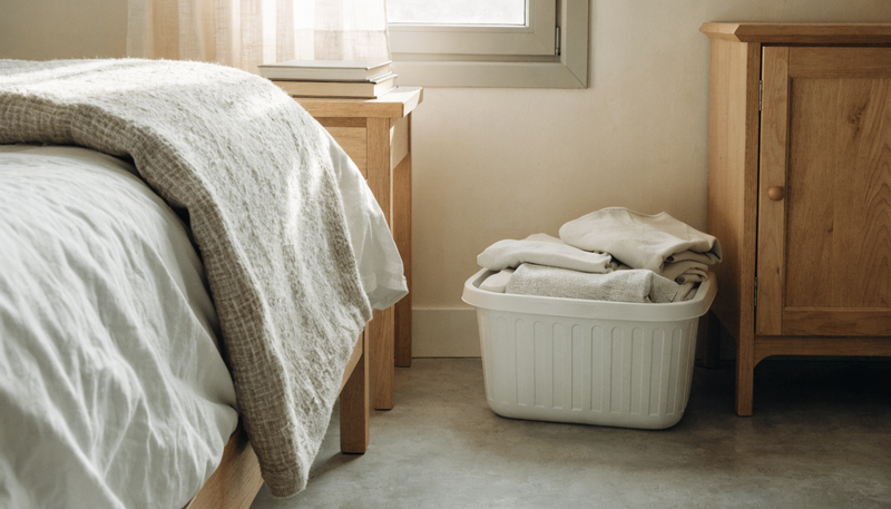 Basket of folded laundry beside a neatly made bed in a calm bedroom