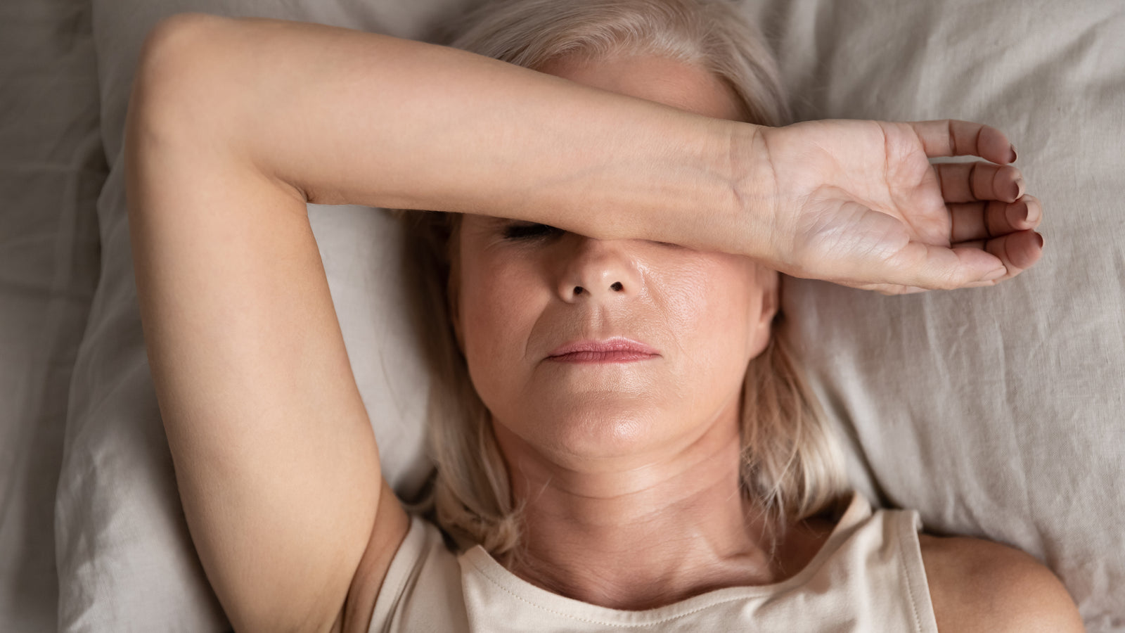 A woman lies on a bed with her arm over her eyes.