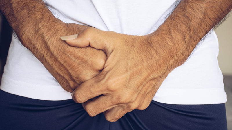 A man clutches his hands in front of his pelvis.