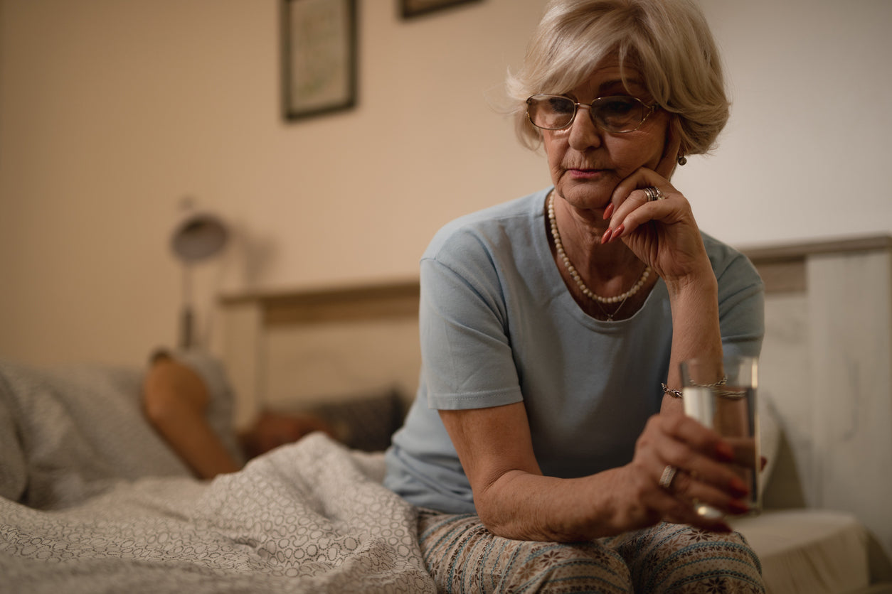 A woman sits up in bed and looks down.