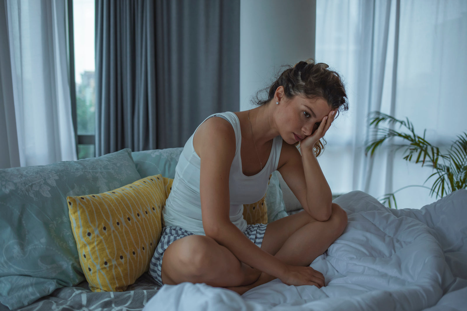 A woman sits on her bed looking upset.