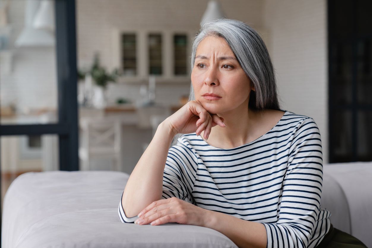 A women leans her head against her hand as she rests on a couch while looking saddened.