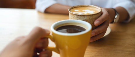 Closeup image of a young couple holding and drinking coffee together in cafe