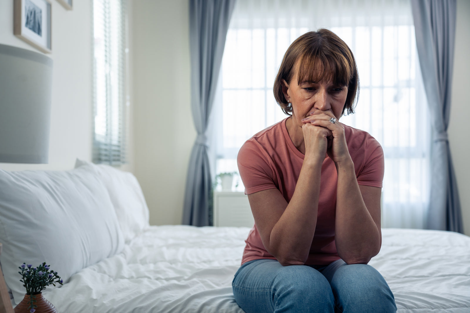 A woman sits on her bed upset. 