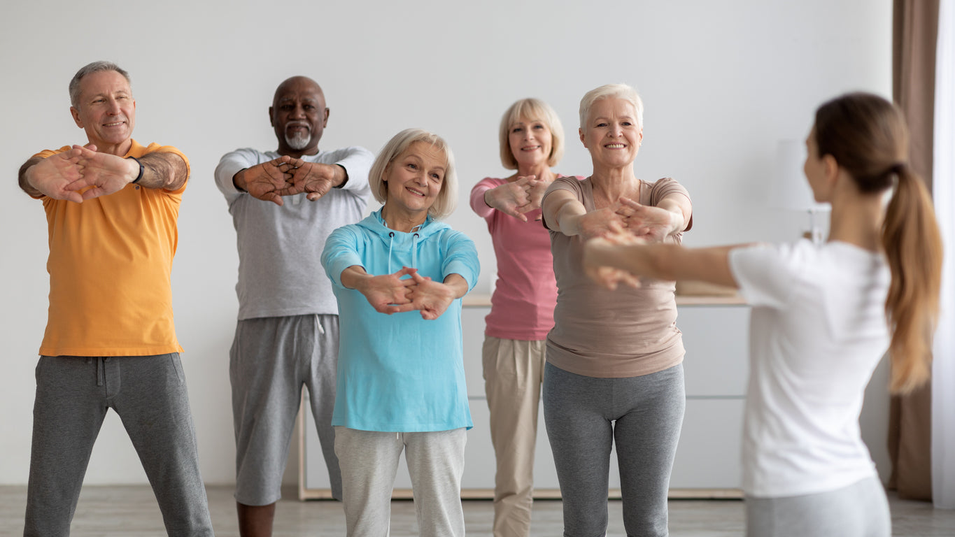 A group of people stretch out their arms before starting a group exercise class.