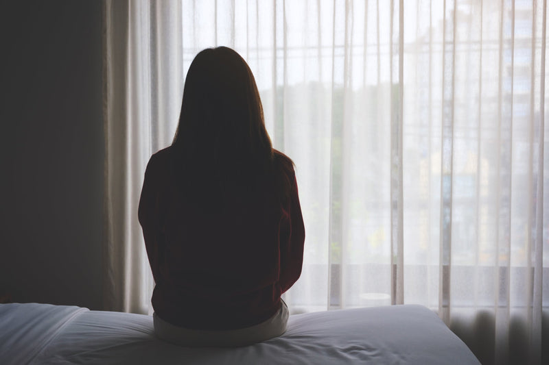 A woman sits on her bed alone in the dark.