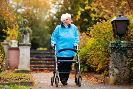 A woman walking with a rollator in a park.