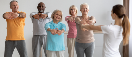 A group of people stretch out their arms before starting a group exercise class.