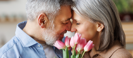 A couple presses their heads together with a bouquet of pink tulips in front of them.