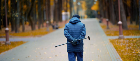 A man walks down a brick path in autumn holding a cane behind him.