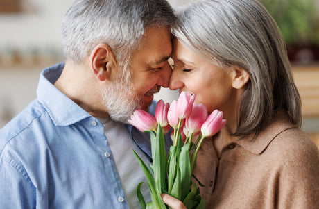 A couple presses their heads together with a bouquet of pink tulips in front of them.