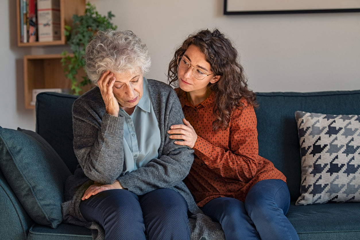 Older woman with her hand to her head sitting next to a younger girl