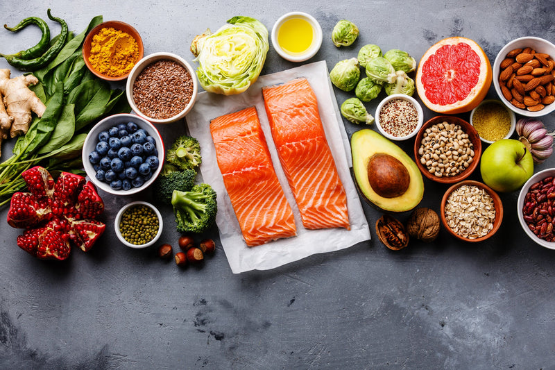 A flatlay of healthy fruits, vegetables, salmon, avocado, and nuts