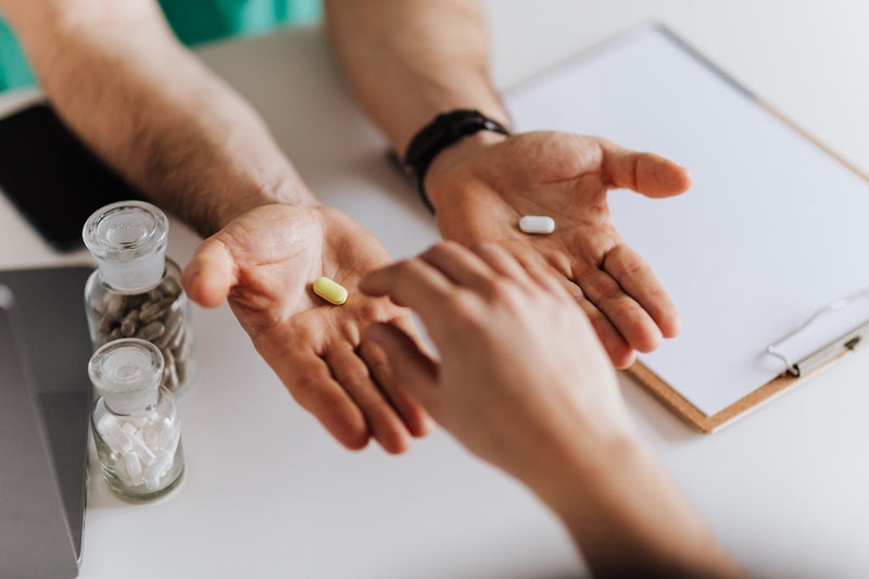 A person holds out two hands each with a different colored pill, another person reaches to choose one.
