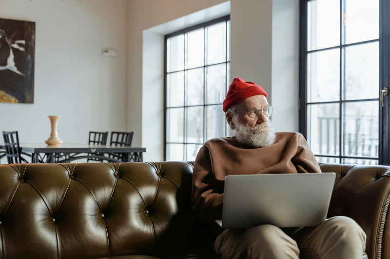 A man sits on a leather couch with a computer in his lap.