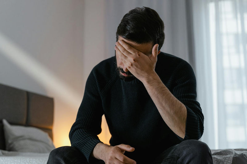 A man sits in bed with his head in his hand.