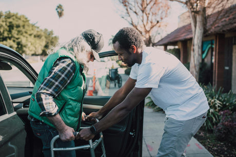 A man helps a man with a walker exit a car safely.