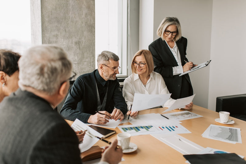 A group of corporate workers discuss papers over a conference table.