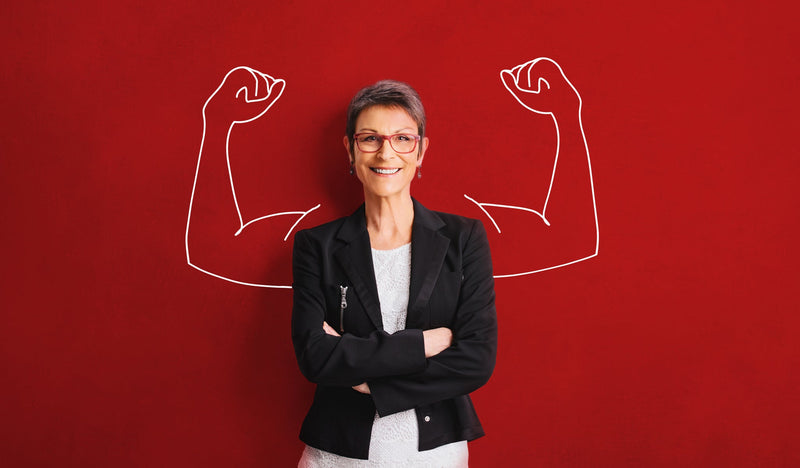 Woman standing against a red backdrop with drawn in arm muscles looking confident