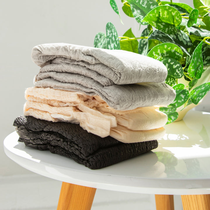 3 colors of Because Maximum Plus underwear stacked on white table beside a plant.