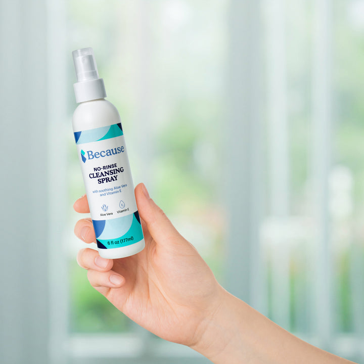 Hand holding a bottle of Because no-rinse cleansing spray with a blurred background