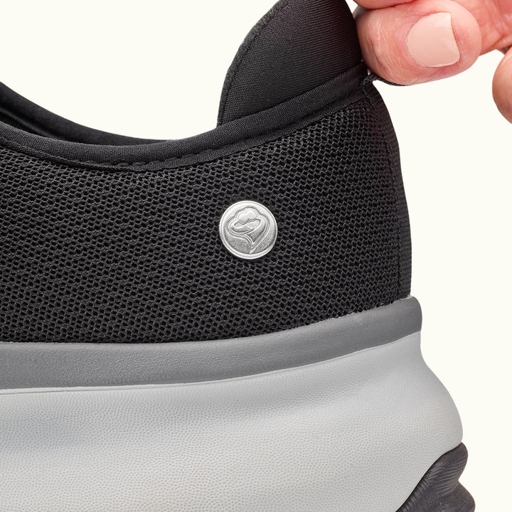 Two fingers holding heel tab on Black Women's Extra Wide Comfort Shoes on a white background
