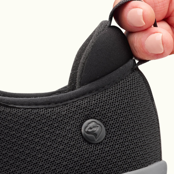 Two fingers holding heel tab on Black Men's Extra Wide Comfort Shoes on a white background